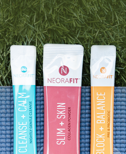 NeoraFit Slim + Skin Collagen Powder, NeoraFit Block + Balance Pre & Probiotic and NeoraFit Cleanse + Calm Nightly Gentle Cleanse sachets laying on a yoga mat atop a field of grass